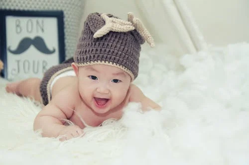 baby wearing a knitted hat laying on a fluffy blanket and laughing