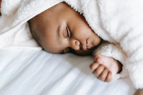 sleeping baby curled in a white bathrobe on a white sheet