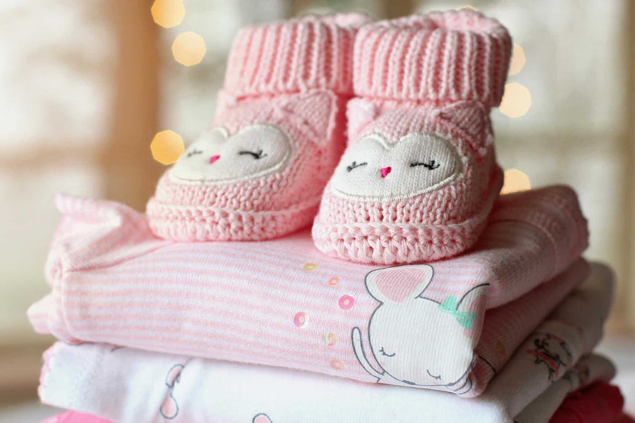 pink baby booties on top of folded clothes