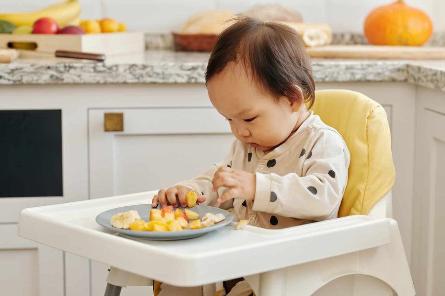 Baby eating fruit on a highchair