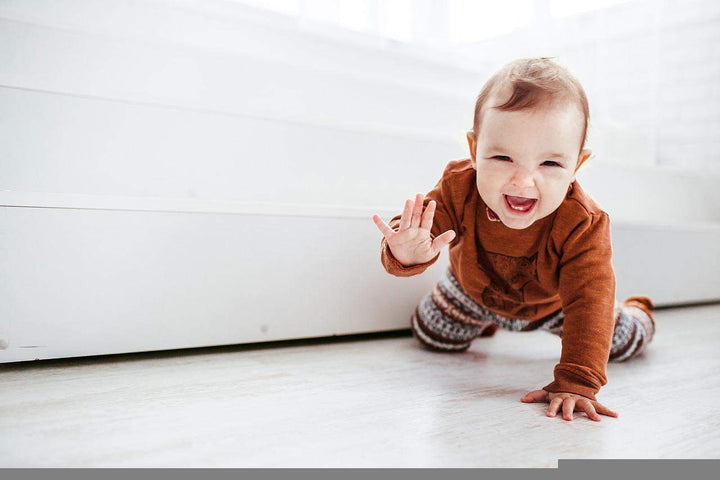 Baby in an orange shirt and striped pants crawling and laughing on a white floor