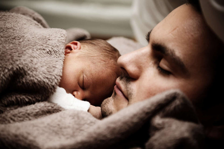 A baby sleeping on their tired parent. 