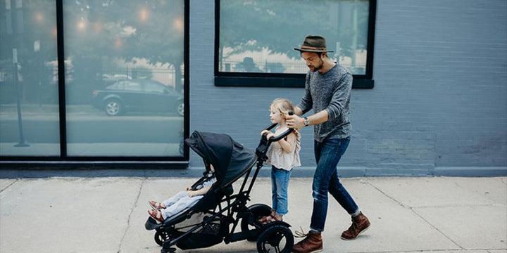 a child riding on a stroller board being pushed by her father