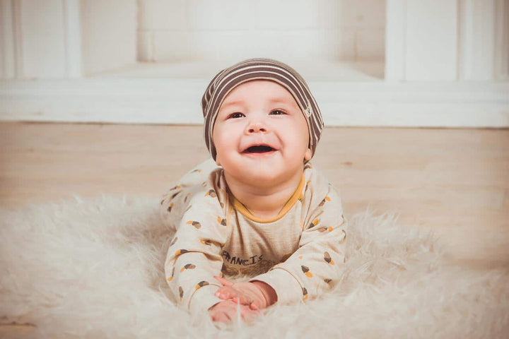 a baby in a yellow onesie laying on the ground and laughing