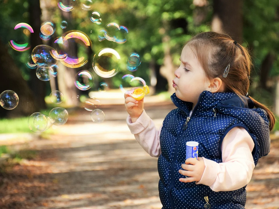 A little girl blowing bubbles outside. 