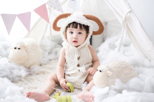 Cute baby dressed like a lamb and surrounded by two plush toy lambs.