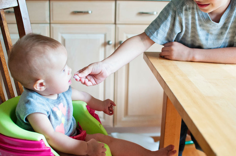 A young boy feeds a baby sitting in a high chair