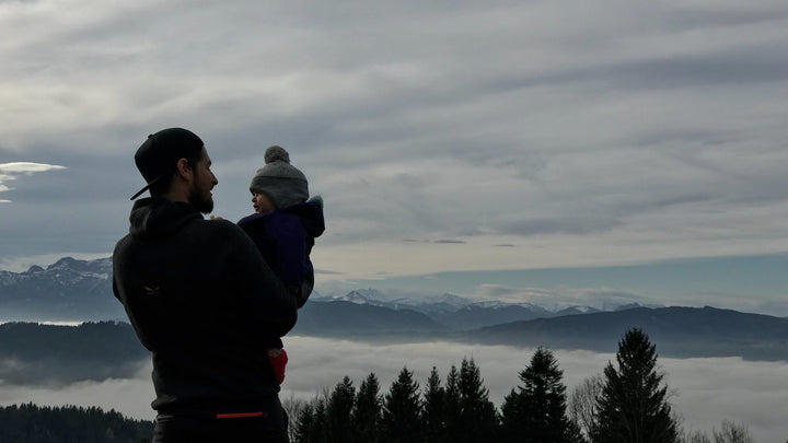 A dad holds his baby, as they overlook cloudy mountains