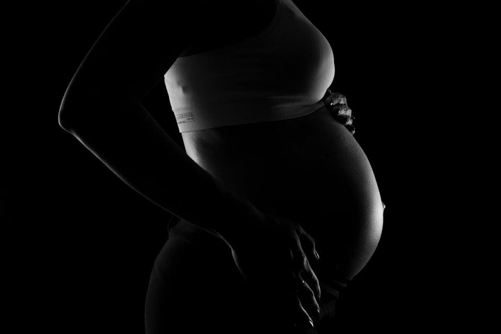A black and gray image show a pregnant woman holding her stomach