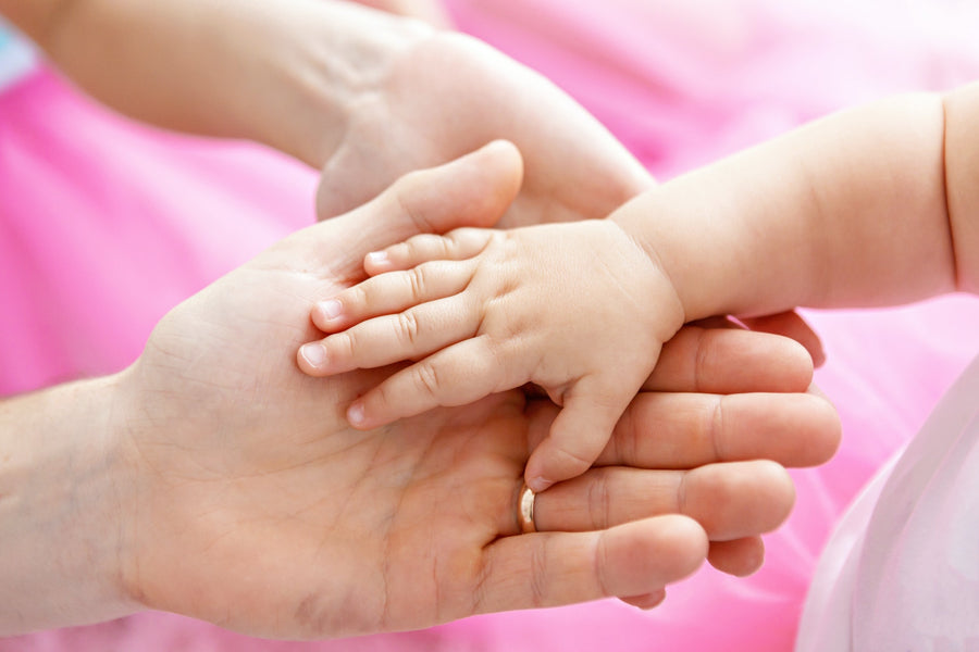 Parents hold their small baby's hand in their palm