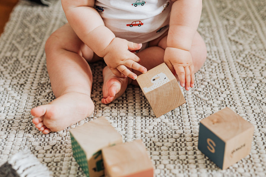 Baby plays with wooden blocks while sitting on the floor