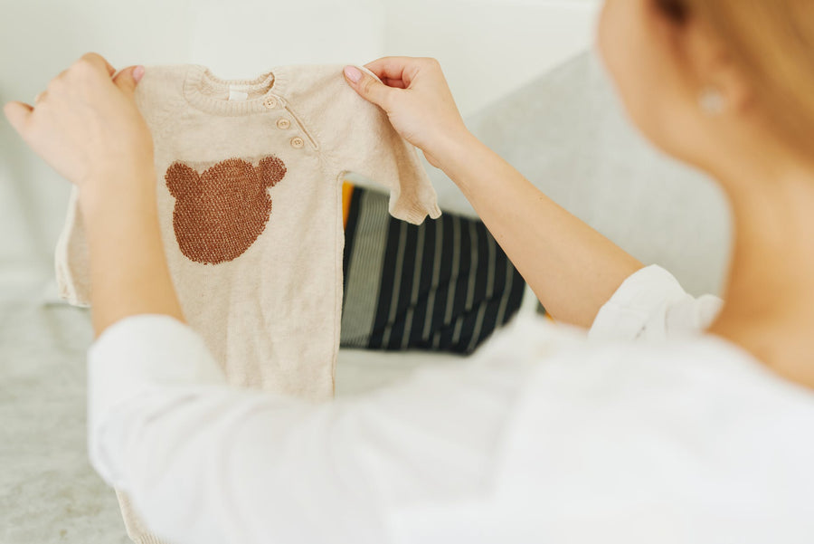 A woman holds up a baby onesie with a fluffy bear face on it.