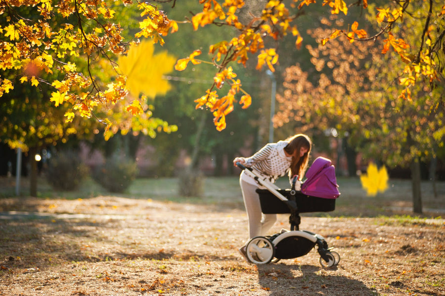 A woman leans over a stroller in the park