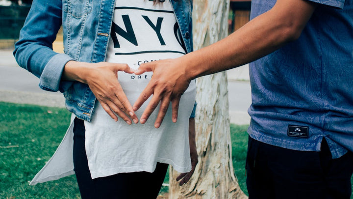 A man and woman form a heart with their hands over the pregnant woman's belly. 