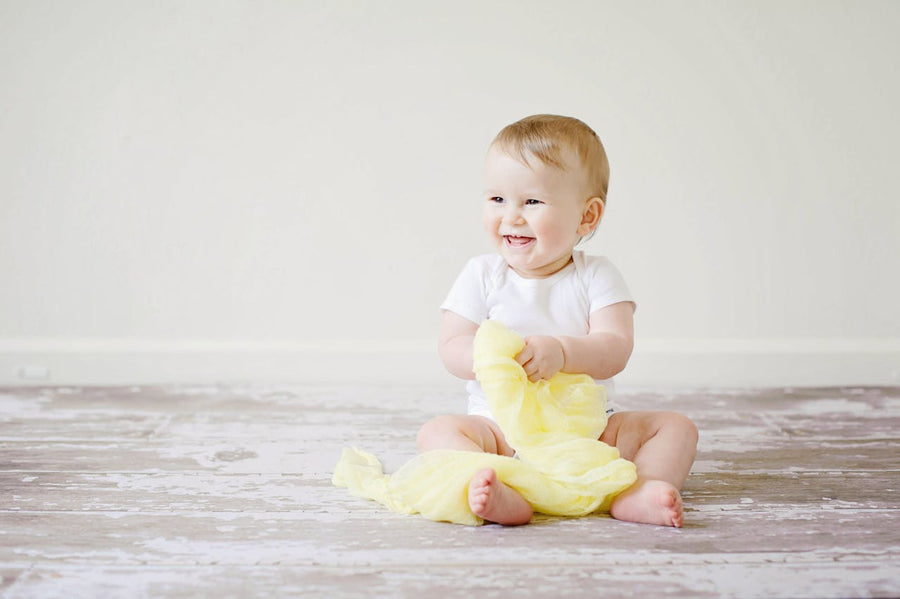  baby holding a yellow blanket smiling