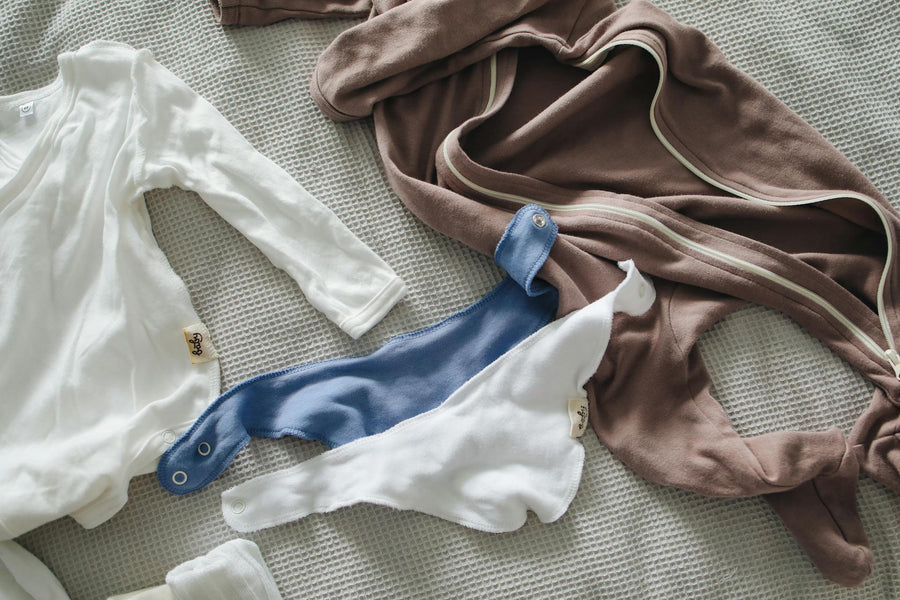An assortment of neutral baby clothes lay on a bed