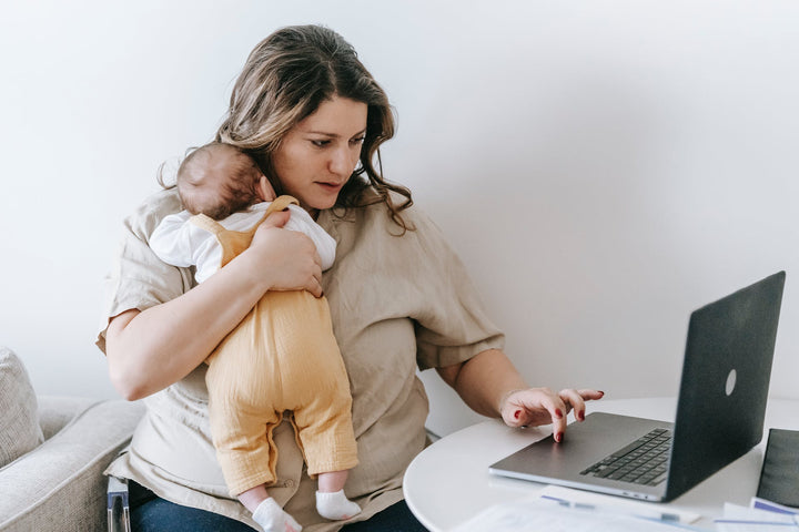 A mom working on a laptop, holds her baby