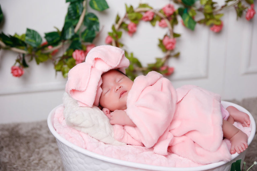 A baby dressed in a pink robe sleeps in a basket