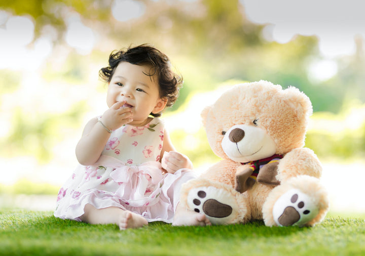 A baby girl sits next to a plush bear  