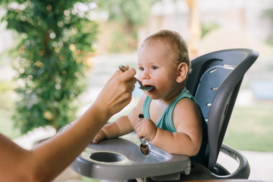 A person out of frame feeds a baby sitting in a high chair