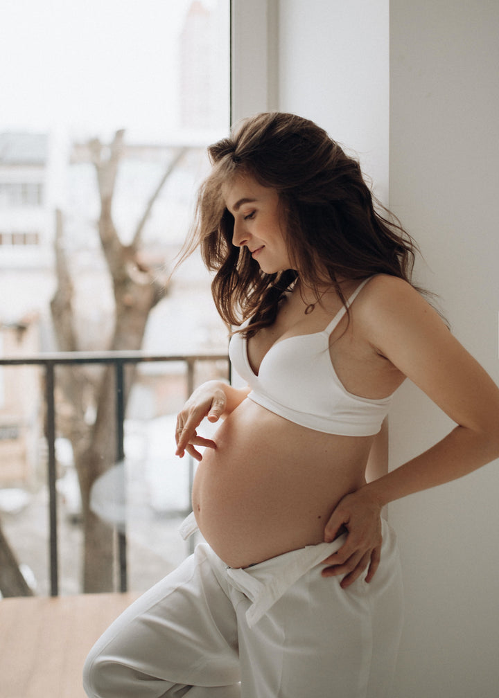 pregnant woman wearing white looking at her stomach