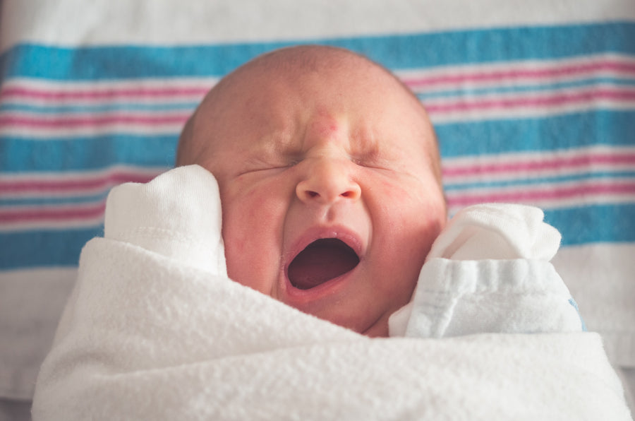 a swaddled baby yawning widely