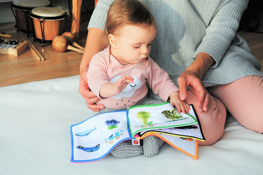 Mother sitting on mat with baby and reading a picture book.